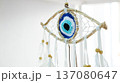 Handmade dreamcatcher amulet with an evil eye nazar woven from natural thread, accented with white feathers and wooden beads, hanging against a bright blue white backdrop 137080647
