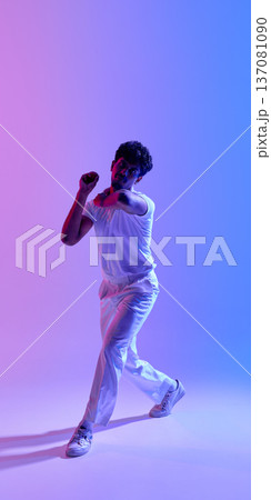 Young male cricket player in bowling action pose under neon gradient light 137081090