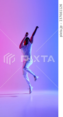 Cricket player jumping in white uniform under pink blue gradient lighting. Cricket player jumping in white uniform under pink blue gradient lighting. 137081126