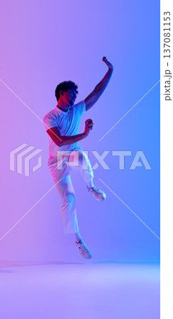 Cricket player jumping under pink and blue gradient lighting wearing white uniform with red ball. Cricket player jumping under pink and blue gradient lighting wearing white uniform with red ball. 137081153