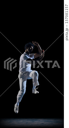 Cricket bowler in mid air delivery on black stage wearing white sports outfit. 137081157