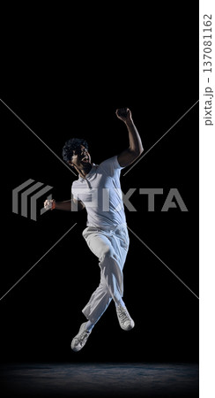 Cricket player celebrating mid air in spotlight on dark studio background wearing white uniform. 137081162