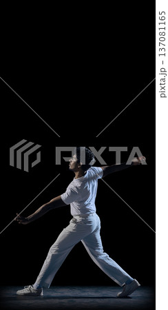 Cricket bowler in dramatic pose on dark background wearing white uniform mid delivery motion. 137081165