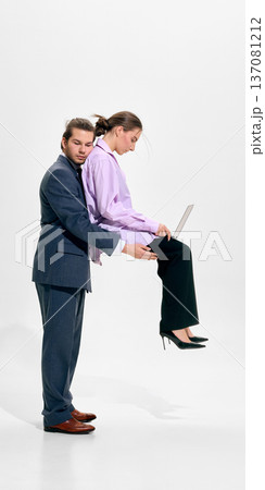 Businessman holding seated businesswoman working on laptop in studio wearing formal attire 137081212
