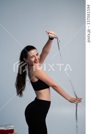 Happy woman with long ponytail posing with a measuring tape, celebrating body goals, fitness journey, weight loss success, and achieving healthy lifestyle results 137081594
