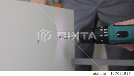 Professional man using an electric drill to adjust a wooden drawer. Furniture installation. Professional man using an electric drill to adjust a wooden drawer. Furniture installation. 137081917