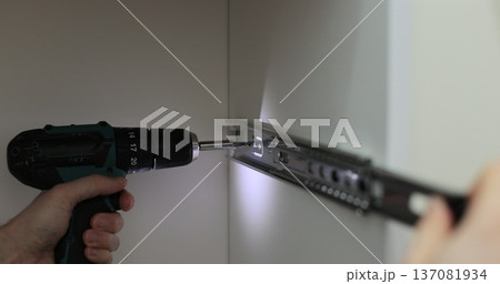 Man using a electric drill to attach a metal drawer slide to a piece of furniture during assembly. Furniture installation. Man using a electric drill to attach a metal drawer slide to a piece of furniture during assembly. Furniture installation. 137081934