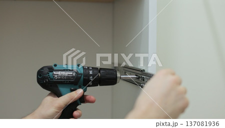 Man using a electric drill to attach a metal drawer slide to a piece of furniture during assembly. Furniture installation. Man using a electric drill to attach a metal drawer slide to a piece of furniture during assembly. Furniture installation. 137081936