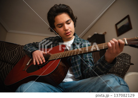Teen Boy Playing Acoustic Guitar at Home in a Cozy Casual Setting Teen Boy Playing Acoustic Guitar at Home in a Cozy Casual Setting 137082129