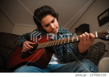 Teenage Boy Playing Acoustic Guitar at Home in Cozy Casual Setting Teenage Boy Playing Acoustic Guitar at Home in Cozy Casual Setting 137082130
