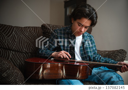 Teenage Boy Playing Acoustic Guitar At Home On Couch, Casual Music Practice In Cozy Interior Teenage Boy Playing Acoustic Guitar At Home On Couch, Casual Music Practice In Cozy Interior 137082145