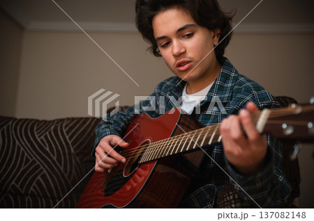 Teenage Boy Playing Acoustic Guitar At Home In Cozy Casual Setting Teenage Boy Playing Acoustic Guitar At Home In Cozy Casual Setting 137082148