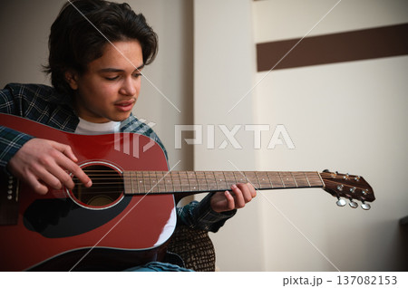 Teenage Boy Playing Acoustic Guitar At Home In Cozy Casual Setting Strumming Music Teenage Boy Playing Acoustic Guitar At Home In Cozy Casual Setting Strumming Music 137082153