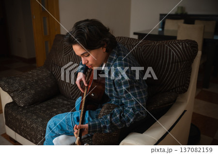 Teenage Boy Playing Acoustic Guitar At Home On Cozy Sofa Casual Music Practice 137082159