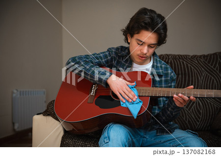Teenage Boy Playing Acoustic Guitar At Home In Casual Clothing While Practicing Music Teenage Boy Playing Acoustic Guitar At Home In Casual Clothing While Practicing Music 137082168