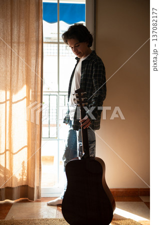Teenage Boy Playing Acoustic Guitar at Home in Cozy Sunlit Interior 137082177