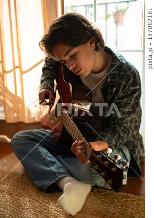 Teenage Boy Playing Acoustic Guitar in Cozy Home Interior 137082181