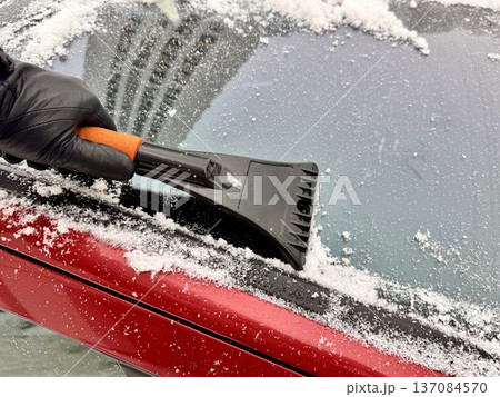 a man cleans a car with a scraper in winter a man cleans a car with a scraper in winter 137084570