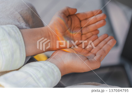 Close-up of childs open hands with soft rainbow light shining across the palms, a dreamy atmosphere Close-up of childs open hands with soft rainbow light shining across the palms, a dreamy atmosphere 137084795