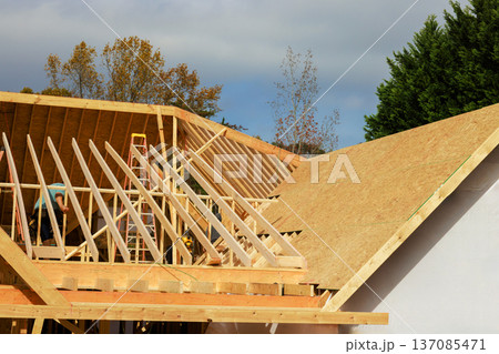 Frame roofing workers install roof frames on house under construction Frame roofing workers install roof frames on house under construction 137085471