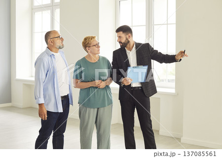 Realtor showing bright modern apartment interior to mature couple during tour 137085561