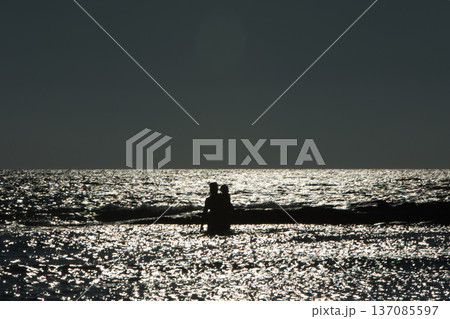 Silhouette of an adult with a child standing in shallow water at sunset in Vlora, Albania, captured on August 25, 2025. The sparkling sea reflects the fading light Silhouette of an adult with a child standing in shallow water at sunset in Vlora, Albania, captured on August 25, 2025. The sparkling sea reflects the fading light 137085597
