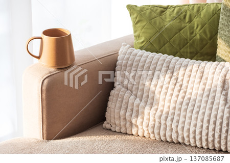 Ceramic Coffee Mug on Sofa Armrest with Textured Pillows. Cozy Home Interior 137085687