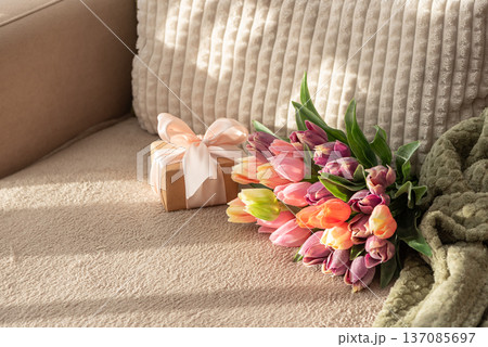 Tulip Bouquet and Gift Box on Cozy Sofa. Warm Spring Flatlay with Soft Textures Tulip Bouquet and Gift Box on Cozy Sofa. Warm Spring Flatlay with Soft Textures 137085697
