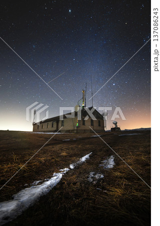 Night sky over a remote communication station with antennas and satellite dishes, surrounded by grass and snow, illuminated by stars and distant city lights Night sky over a remote communication station with antennas and satellite dishes, surrounded by grass and snow, illuminated by stars and distant city lights 137086243