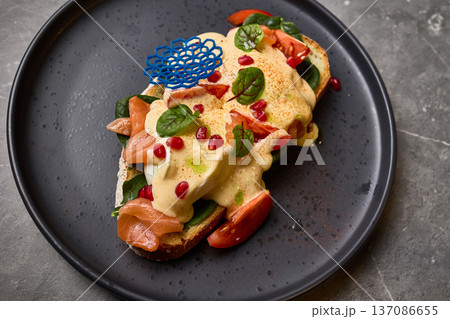 Delicious open-faced sandwich with smoked salmon, creamy sauce, fresh spinach, vibrant pomegranate seeds on dark plate, gourmet meal concept Delicious open-faced sandwich with smoked salmon, creamy sauce, fresh spinach, vibrant pomegranate seeds on dark plate, gourmet meal concept 137086655