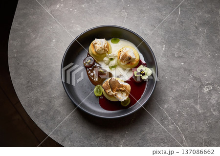 Elegant dessert with meringue, grapes, cream, garnished with flower on black plate over marble table culinary art concept 137086662