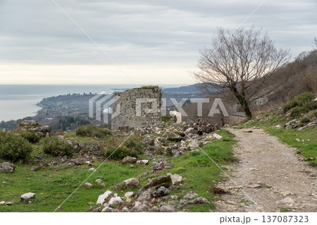 Anakopia fortress ruins, mountain trail, Black Sea coastline view, stone tower fragment and green hillside under cloudy sky in Abkhazia. Travel marketing, cultural tourism campaigns, outdoor lifestyle Anakopia fortress ruins, mountain trail, Black Sea coastline view, stone tower fragment and green hillside under cloudy sky in Abkhazia. Travel marketing, cultural tourism campaigns, outdoor lifestyle 137087323
