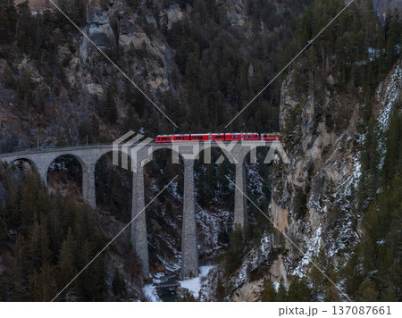 Landwasser Viaduct in Graubunden, Switzerland, shows Glacier Express crossing six arches above a rocky gorge, amid forested cliffs and lingering snow in late winter. Landwasser Viaduct in Graubunden, Switzerland, shows Glacier Express crossing six arches above a rocky gorge, amid forested cliffs and lingering snow in late winter. 137087661