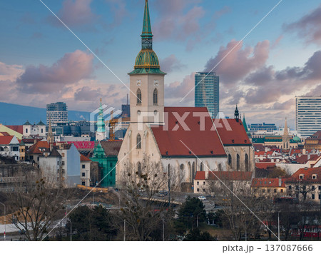 Bratislava, Slovakia, centers on St. Martin's Cathedral and tall spire, framed by modern high rises, winter trees, and a curving roadway in soft late afternoon light. Bratislava, Slovakia, centers on St. Martin's Cathedral and tall spire, framed by modern high rises, winter trees, and a curving roadway in soft late afternoon light. 137087666