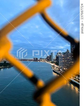 Dusk settles on the East River in New York City, with Manhattan on the right, Roosevelt Island ahead, winter tones on water and sky, and fence bokeh framing the scene. 137087724