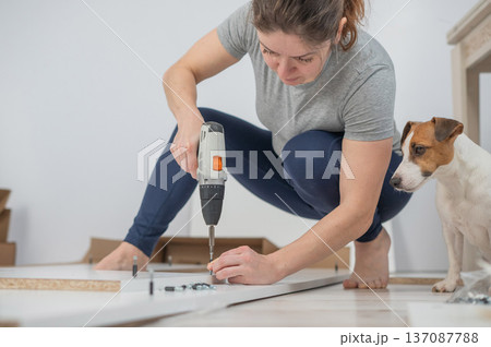 A Caucasian woman uses a screwdriver to tighten a screw while assembling a cabinet. A Caucasian woman uses a screwdriver to tighten a screw while assembling a cabinet. 137087788