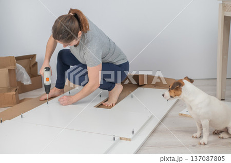 A Caucasian woman uses a screwdriver to tighten a screw while assembling a cabinet. 137087805