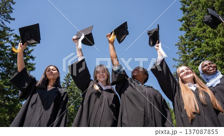 Young women of different nationalities pull graduation caps up. Young women of different nationalities pull graduation caps up. 137087855