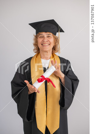 Happy senior woman in graduation gown holding diploma on white background. Happy senior woman in graduation gown holding diploma on white background. 137087901