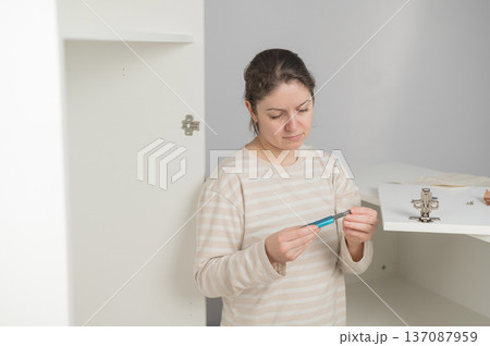 A Caucasian woman assembles a wardrobe. She understands the hardware. 137087959