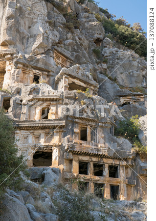 A breathtaking view of ancient Lycian rock-cut tombs embedded in a rugged cliffside in Demre, Turkey. The historic tombs showcase intricate stone architecture, blending seamlessly with the natural A breathtaking view of ancient Lycian rock-cut tombs embedded in a rugged cliffside in Demre, Turkey. The historic tombs showcase intricate stone architecture, blending seamlessly with the natural 137088124