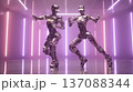 Two humanoid robot figures with metallic surfaces pose dynamically in a futuristic setting illuminated by colorful neon lights and reflective flooring 137088344