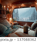 Cozy interior of a camper van with plush cushions, a steaming mug on a table, and a snowy mountain landscape visible through the large window 137088362