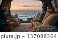 Cozy interior of a vehicle with plush cushions and blankets overlooking a scenic ocean sunset, featuring decorative elements like lanterns and baskets 137088364