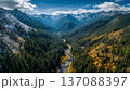 Aerial view of a winding river flowing through a lush green valley surrounded by snow-capped mountains and dense forests under a clear blue sky 137088397