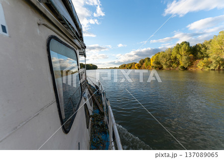 Boat travels along a river surrounded by trees on a clear day with clouds in the sky 137089065