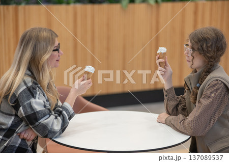 A mother and her teenage daughter eat ice cream at a shopping mall food court. 137089537