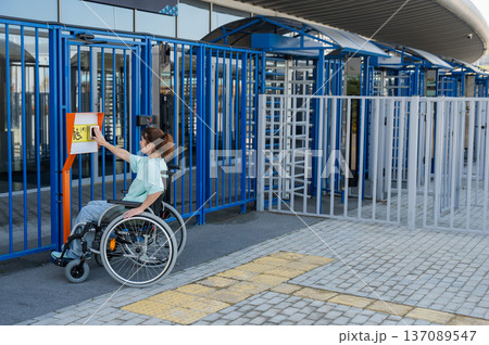 A woman in a wheelchair uses a touch-sensitive Braille help button.. A woman in a wheelchair uses a touch-sensitive Braille help button.. 137089547