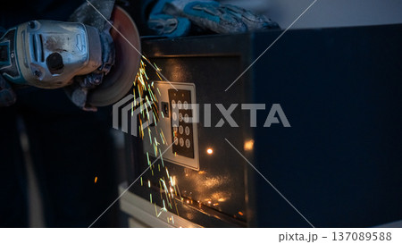 A man breaks into a safe with a grinder. 137089588