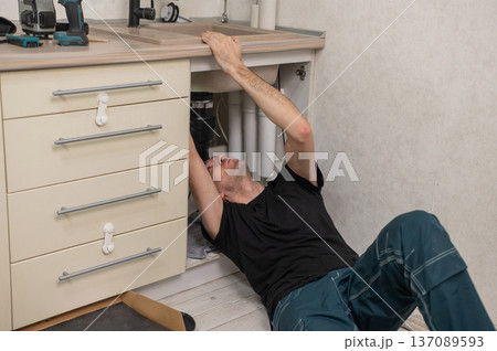 A plumber is replacing a faucet in the kitchen. A plumber is replacing a faucet in the kitchen. 137089593